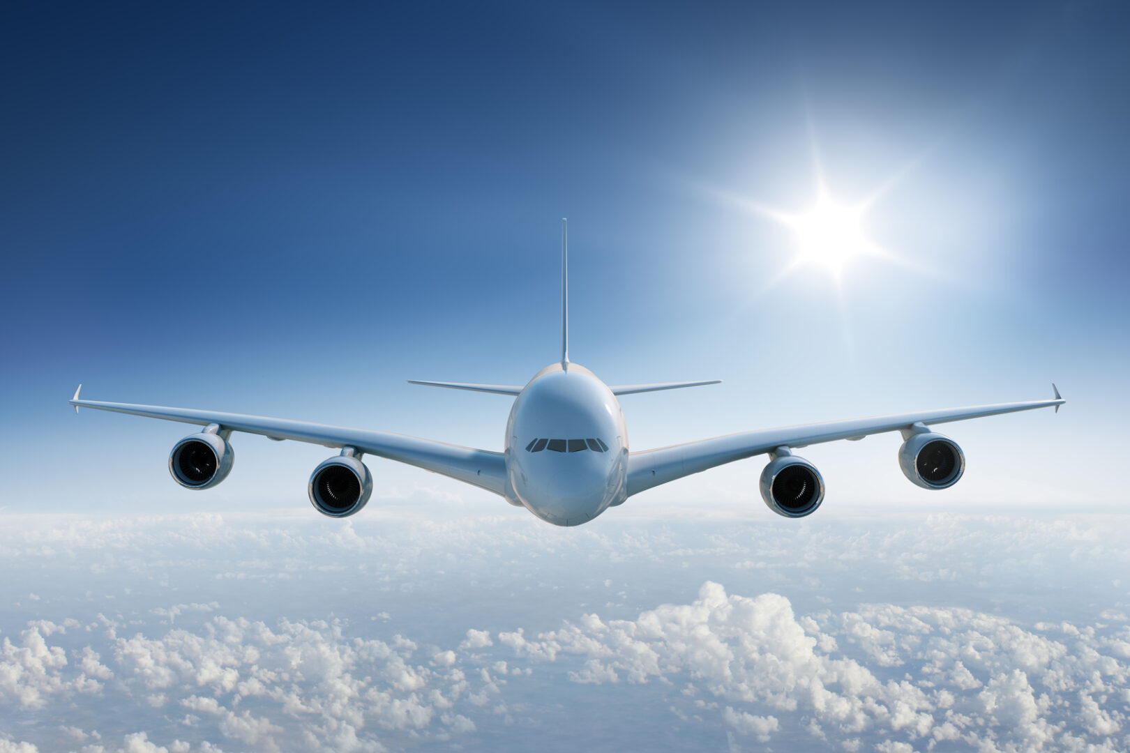 Big airplane flying above the clouds, towards the camera with the sun in blue sky